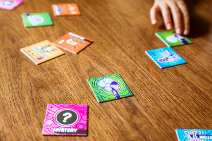 Colorful game cards on a wooden table with a hand reaching for one of them.