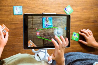 Children playing a augmented reality game on a tablet with cards on a wooden table.