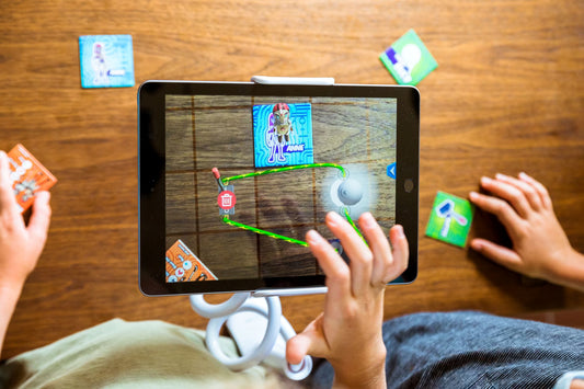 Children playing a augmented reality game on a tablet with cards on a wooden table.