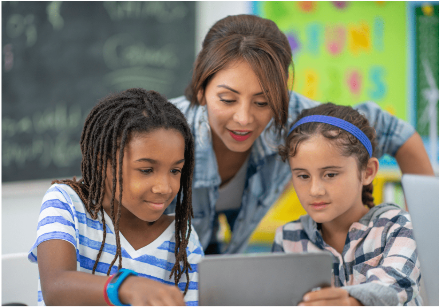 teacher helping 2 students who are sharing an ipad.